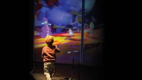 Young boy walking alongside a vibrant screen displaying beautiful colors. On the screen, multiple artists with instruments create a captivating visual spectacle