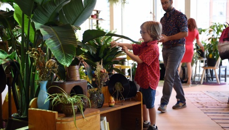 One child touching a plant surrounded by many others, with a few adults standing in the background.
