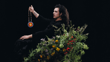 Jeremy Dutcher holding an indigenous necklace and standing in a bush