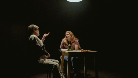 Two seated individuals conversing at a table in a dimly lit room.