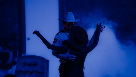Under an azure glow, two individuals adorned with cowboy hats twirl in a dance. 