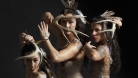 Three women with feather in their hair are posed holding deer antlers in front of their faces.   