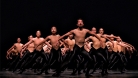 A large group of dancers on stage in black tights and skin toned tops, with arms floating up. ©  Michael Slobodian