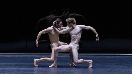 2 male dancers with bare chests and skin toned shorts locked in an athletic embrace. 