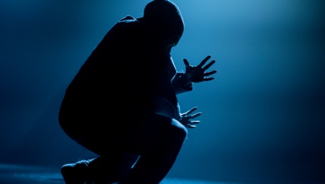 One dancer crouches on the stage with fingers outreached in silhouette. 