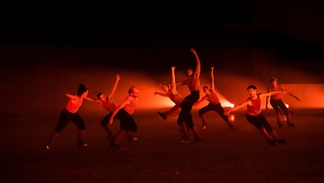 8 performers on skates in various poses with red lighting.