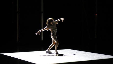 A young performer with arms outstretched on an elevated square stage. 