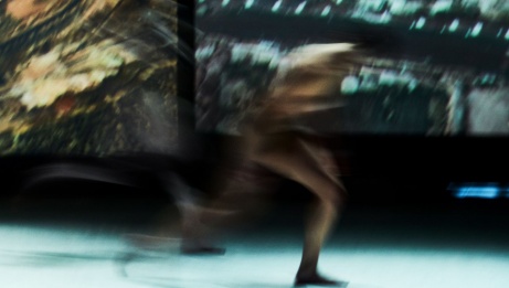 A blurry image of a dancer in motion in front of a projected photograph. 