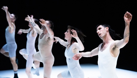 5 dancers in a line, wearing light toned unitards balance on one leg with arms hovering. 