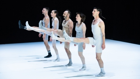 Five dancers in light toned unitards stand in a line, each with one leg extended forward.  