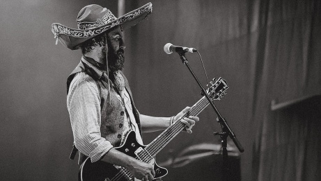 Quique Escamilla, artist, performing on stage with his guitar, wearing a sombrero. 