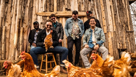 Les six membres du groupe musical Beauxmont, souriants parmi des poules, devant une grange.  © Debout gauche à droite : Jonathan Mpunge, Patrick Dugas, Justin Doucet, Chris Cormier, Felix Belliveau et Jesse Mea. 