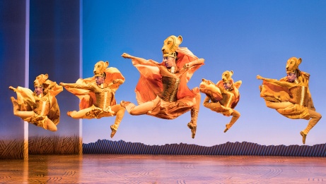 A group of women, all with wooden lioness masks attached to their heads, leap into the air performing their Lioness Dance.