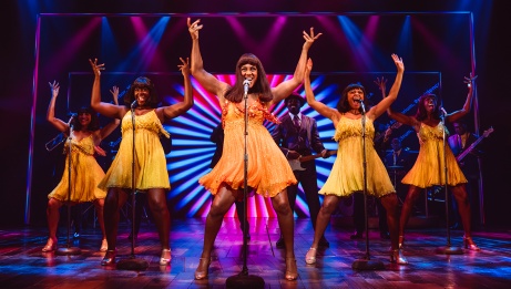 Vêtue d’une robe jaune, Tina se tient debout au centre de la scène et chante avec les deux mains en l’air. Elle est entourée de deux choristes qui portent la même robe et prennent la même pose.