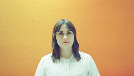 Ellen Froese, on an orange background, looking at the camera 