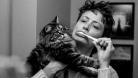 Mo Kenney brushing their teeth while holding their cat. 