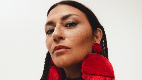Elisapie looking down at the camera, wearing large red earrings. © Leeor Wild