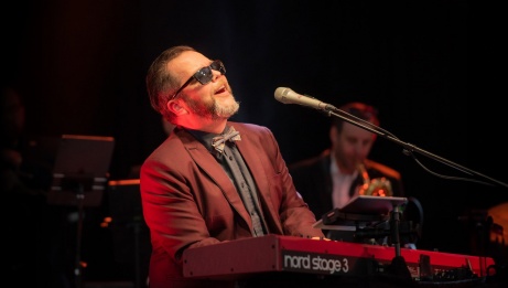 Jeff Rogers with a suit and sunglasses playing keyboard and signing.