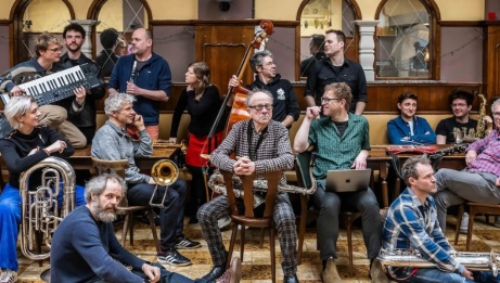 Tout l'orchestre dans une pièce, regardant partout ! L'image est un peu désordonnée avec beaucoup de gens partout.