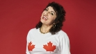 Steph smiling, wearing a white t-shirt with maple leaves and she's in front of a red wall. 