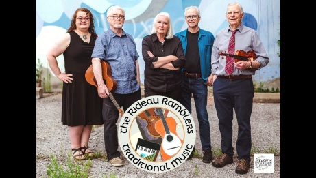 The five members of the Rideau Ramblers outside. A member is holding his guitar and another member is holding his violin.