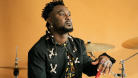 Donald Dogbo sitting next to his drums on an orange background. © Marion Chuniaud