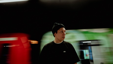 A man is wearing a beanie in front of a blurry moving train.