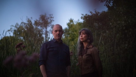 Sarah Pagé and Patrick Graham are standing near a hill. They are looking off into the distance. 