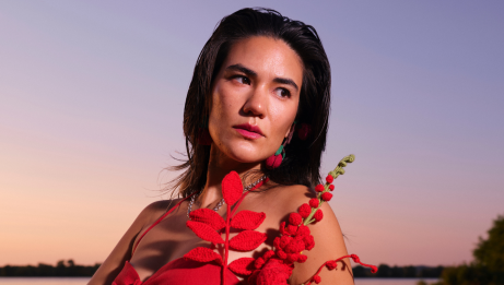 Yolande Laroche tenant un bouquet de fleurs tricotées. Elle se tient devant un lac au coucher du soleil.