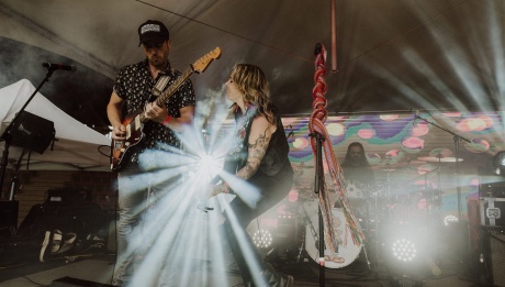 Amanda Rheaume performing on stage. She's playing the guitar next to a bass player. There is a flash of light behind them.