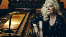 Judy Collins sitting by a piano. 