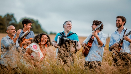 Six instrumentistes se tiennent joyeusement debout dans un champ de hautes herbes. Ils jouent plusieurs instruments, dont de la guitare, de l&rsquo;accord&eacute;on, de la mandoline et du tambourin. 