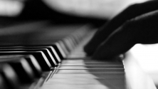 Gros plan en noir et blanc sur la main d'une personne jouant sur les touches d'un piano. 