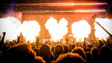 Une foule nombreuse assiste &agrave; un concert, tandis que des flammes jaillissent de la sc&egrave;ne, renfor&ccedil;ant l'intensit&eacute; du spectacle. 